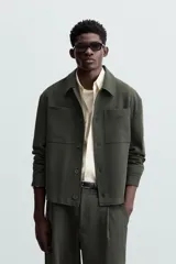 Sobrecamisa negra de corte amplio, con cuello solapa, manga larga con puños abotonados, bolsillos de parche en el pecho, bolsillos laterales y cierre frontal con botones.