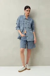 Sobrecamisa oversize de jean azul con cuello camisero, cierre frontal con botones, mangas largas y bolsillos de parche en el pecho.