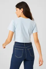 Remera cropped negra de algodón con cuello redondo y estampado de hojas blancas en el hombro.