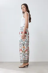 Pantalón de vestir blanco con estampado floral en tonos naranja, verde y rojo. Presenta un corte recto y cintura elástica. Incluye una chaqueta haciendo juego.