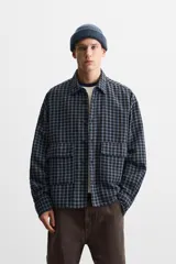 Camisa de hombre a cuadros azules y negros, de corte cuadrado, con cuello solapa, manga larga con puños abotonados, cierre frontal con botones y bolsillos de parche con solapa en el pecho.