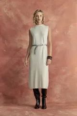 Vestido midi color beige, sin mangas y cuello alto. Incluye cinturón de cadena plateada y botas de cuero marrones.