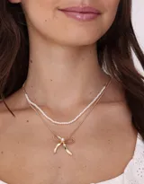 Collar corto doble, con cadena superior de perlas y cadena inferior dorada con dije de moño.