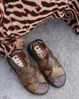 Sandalias marrones de cuero vacuno con tiras cruzadas y suela plana negra.