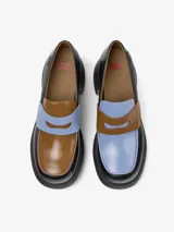 Mocasín de cuero vacuno con diseño bicolor en negro y marrón, destacando una banda frontal en color celeste. Presenta un tacón grueso y plataforma de goma, con plantilla de EVA para mayor amortiguación.