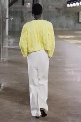 Chaqueta corta color amarillo pastel con textura de volantes, cuello redondo, manga larga y cierre frontal con botón a presión oculto.