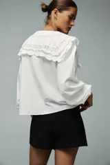 Camisa blanca de popelín de algodón con cuello redondo con tejido en superposición a tono y aplicación de bordados. Manga larga acabada en elástico y cierre frontal con botones ocultos por sopata.
