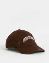 Gorra de béisbol marrón con bordado frontal de la leyenda "New York" en blanco. Presenta detalles de roturas en la visera y la corona.