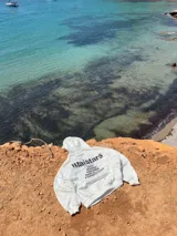 Buzo canguro con capucha, color blanco con estampado de camuflaje en tonos grises. Estampado en la espalda con el logo de la marca y nombres de ciudades.