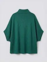 Capa o poncho tejido color verde esmeralda, con cuello polera alto que se cierra con un botón grande en el lateral. Presenta mangas cortas estilo japonesa y un calce amplio.