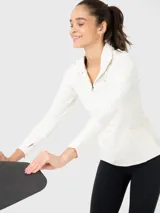 Buzo deportivo blanco de tela suave y delgada con medio cierre frontal, mangas largas con orificios para los pulgares y logo en el pecho.