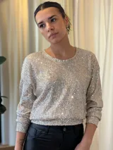 Blusa de lentejuelas plateadas, de manga larga y cuello redondo.