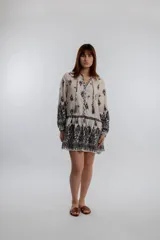 Vestido corto color crema con estampado de flores y arabescos en negro, escote redondo con lazo y borlas, mangas largas con puños elásticos y corte evasé.
