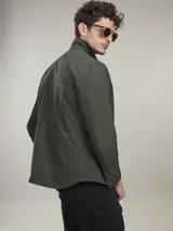 Camisa verde militar de manga larga con cierre de botones, cuello clásico y dos bolsillos frontales con solapa.