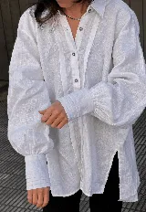 Camisa blanca oversize de lino con corte estilizado, tablas visibles en el frente y canesú con alforzas en la espalda. Manga larga abullonada con puños altos. Cierre frontal con botones.
