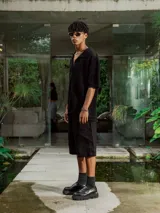 Camisa de manga corta color crudo/blanco, confeccionada en tejido de punto abierto con textura calada y cuello polo. Presenta cierre frontal de botones.