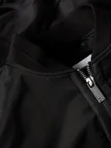 Campera bomber negra Calvin Klein de satén de nailon reciclado, con cuello, puños y bajo de punto de canalé. Tiene cierre de cremallera, bolsillos de hendidura en la cintura, detalle de cremallera en la manga e insignia con el logo de goma de Calvin Klein en la manga. El forro y el relleno son de poliéster reciclado REPREVE®.