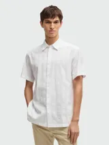 Camisa blanca de manga corta con cuello clásico y botones frontales. Presenta un tejido texturizado con finas rayas verticales en relieve.