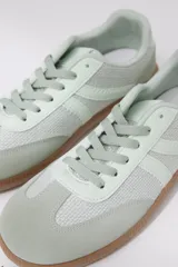 Zapatilla deportiva color beige con detalles de diseño textil y suela de goma.