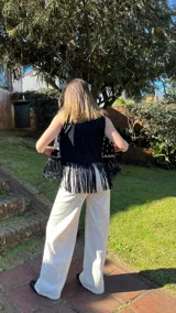 Chaleco negro de gamuza con flecos y bordados blancos en el frente.