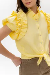 Camisa de lino color lila con volados en el cuello y en las mangas cortas abullonadas. Presenta un diseño de corte recto con cierre frontal de botones.