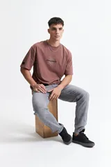 Remera marrón de manga corta con fit oversize, cuello redondo y estampado con texto en el frente.