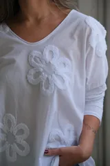 Remera blanca de mangas largas con cuello redondo y apliques de flores blancas en relieve.