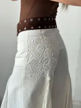 Pantalón blanco de corte palazzo con aplicaciones de encaje floral en los laterales.