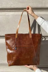 Bolso grande tipo tote de cuero color marrón con costuras decorativas en los laterales, forro interior con bolsillo para celular y bolsillo con cierre. Incluye bolsillo trasero con cierre y correas largas para colgar del hombro.