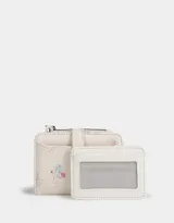 Billetera pequeña de cuerina color crema con estampado de flores y lazos. Tiene cierre superior y broche con botón para cerrar.