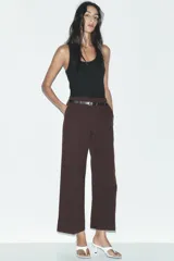Pantalón marrón de tiro alto con cinturón negro, bolsillos delanteros y cierre frontal con cremallera y gancho metálico.
