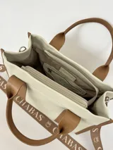 Bolso tote color crema con detalles en cuero marrón. Tiene doble asa de mano y correa de hombro extraíble con el logo de la marca.