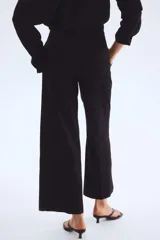 Pantalón sastrero tobillero negro de tiro alto con cierre y pretina prolongada con botón. Presenta bolsillos al bies, bolsillos traseros decorativos y piernas amplias con pliegues adelante y atrás.