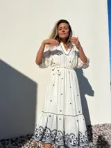 Vestido largo blanco con bordados azules, escote en V, mangas 3/4 abullonadas y lazo en la cintura.