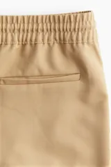 Pantalón palazzo color beige con cintura elástica fruncida y cordón ajustable. Cuenta con bolsillos laterales discretos y bolsillos traseros decorativos.