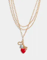 Collar dorado de tres hilos con dijes colgantes: corazón rojo con strass, trébol dorado, herradura dorada con logo de la marca y vaquita de San Antonio celeste con lunares blancos.