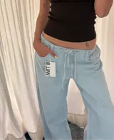 Pantalón jean celeste a rayas verticales blancas, de corte ancho y cintura con cordón ajustable.