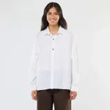 Camisa blanca de corte oversize, con cuello clásico, mangas largas y cierre frontal con botones fantasía dorados.