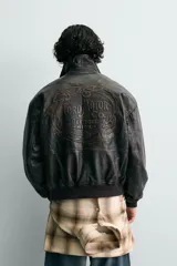 Cazadora bomber de piel color marrón oscuro envejecido, con cuello solapa, cierre frontal de cremallera y puños y bajo en rib elástico. Presenta grabados en relieve en el delantero y la espalda.