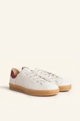 Zapatillas bajas blancas de cuero vacuno con detalle de refuerzo de gamuza color borgoña en el talón y suela de goma color caramelo.