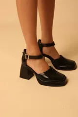 Sandalias negras de charol con plataforma, taco geométrico y pulsera al tobillo con hebilla metálica.