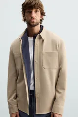 Sobrecamisa negra de tejido con elasticidad, cuello solapa, manga larga con puño abotonado, bolsillos de plastrón en el pecho y cierre frontal con botones a presión.