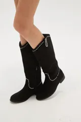 Botas texanas negras de caña media, confeccionadas en gamuza. Presentan un diseño de estilo western con detalles de tachas metálicas plateadas decorando el borde superior y el contorno del empeine. Tienen un taco bajo y punta ligeramente afilada.