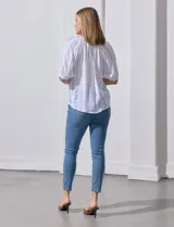 Blusa blanca de algodón marca Zac & Rachel, con cuello a la base, escote en V, abertura central con botones y sisa con aplique calado.