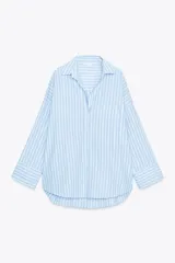 Camisa celeste y blanca a rayas verticales, de corte amplio, con cuello solapa, escote pico, manga larga con puños abotonados, bolsillo en el pecho y bajo asimétrico con aberturas laterales. Cierre frontal con botones.
