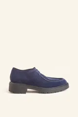 Zapato tipo wallabee de gamuza azul con costuras blancas a la vista y suela de goma negra con plataforma.