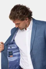Saco azul de lino, corte clásico, con solapa de muesca, cierre de dos botones, bolsillo en el pecho y bolsillos laterales con solapa.