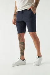 Bermuda color beige, de corte chino clásico, con bolsillos laterales y traseros, cierre con botón y cremallera, presillas para cinturón y logo bordado. Confeccionada en algodón y spandex.