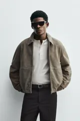 Cazadora de hombre color verde oliva, confeccionada en piel con acabado ante. Presenta un corte boxy fit, cuello solapa, cierre frontal de cremallera, bolsillos delanteros y elásticos en puños y bajo.