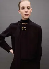 Blusa azul con lazo al cuello, de tejido fluido y satinado, con cierre oculto de botones y mangas largas abotonadas.